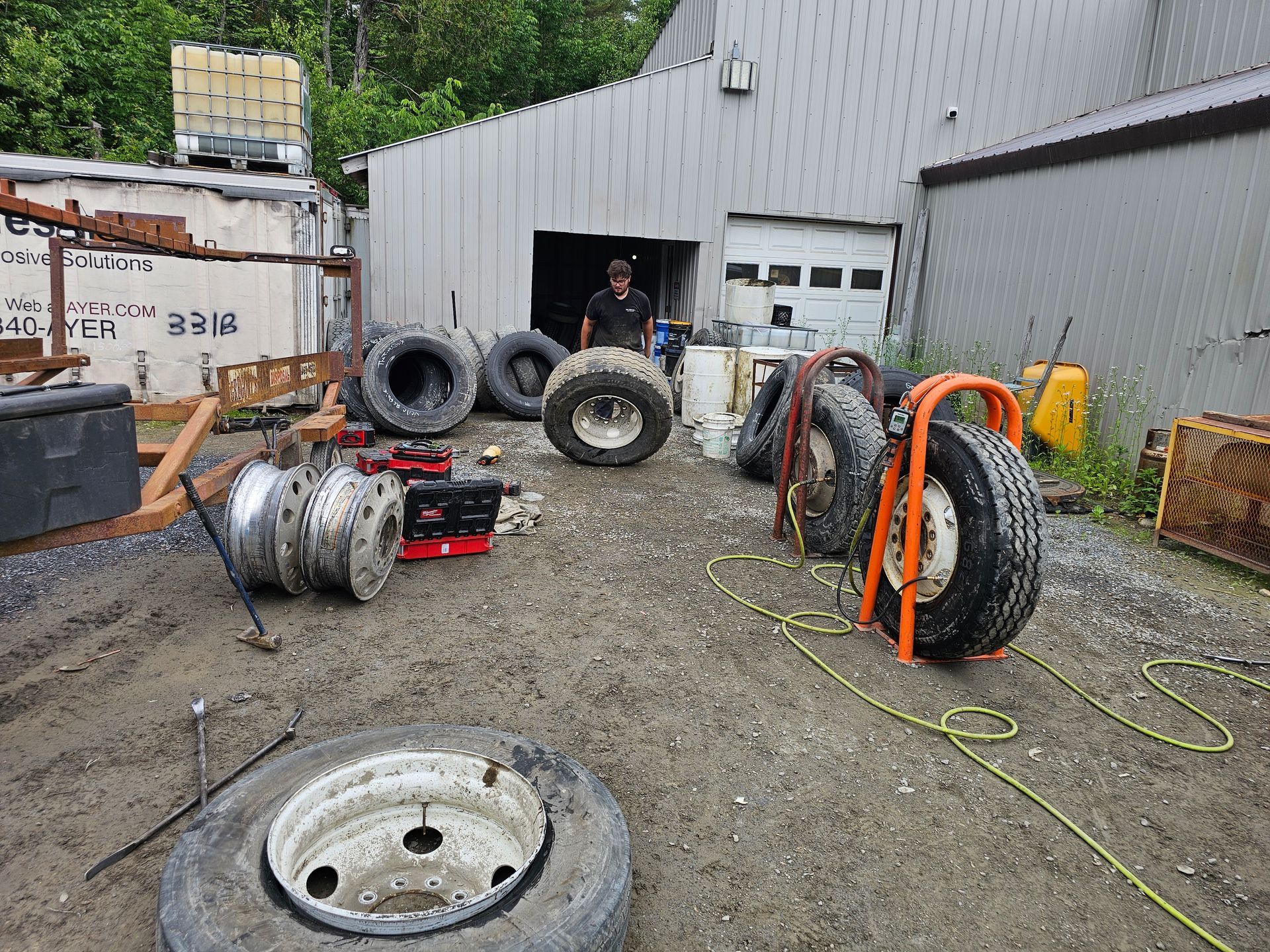 A man is standing in a garage surrounded by tires and wheels.