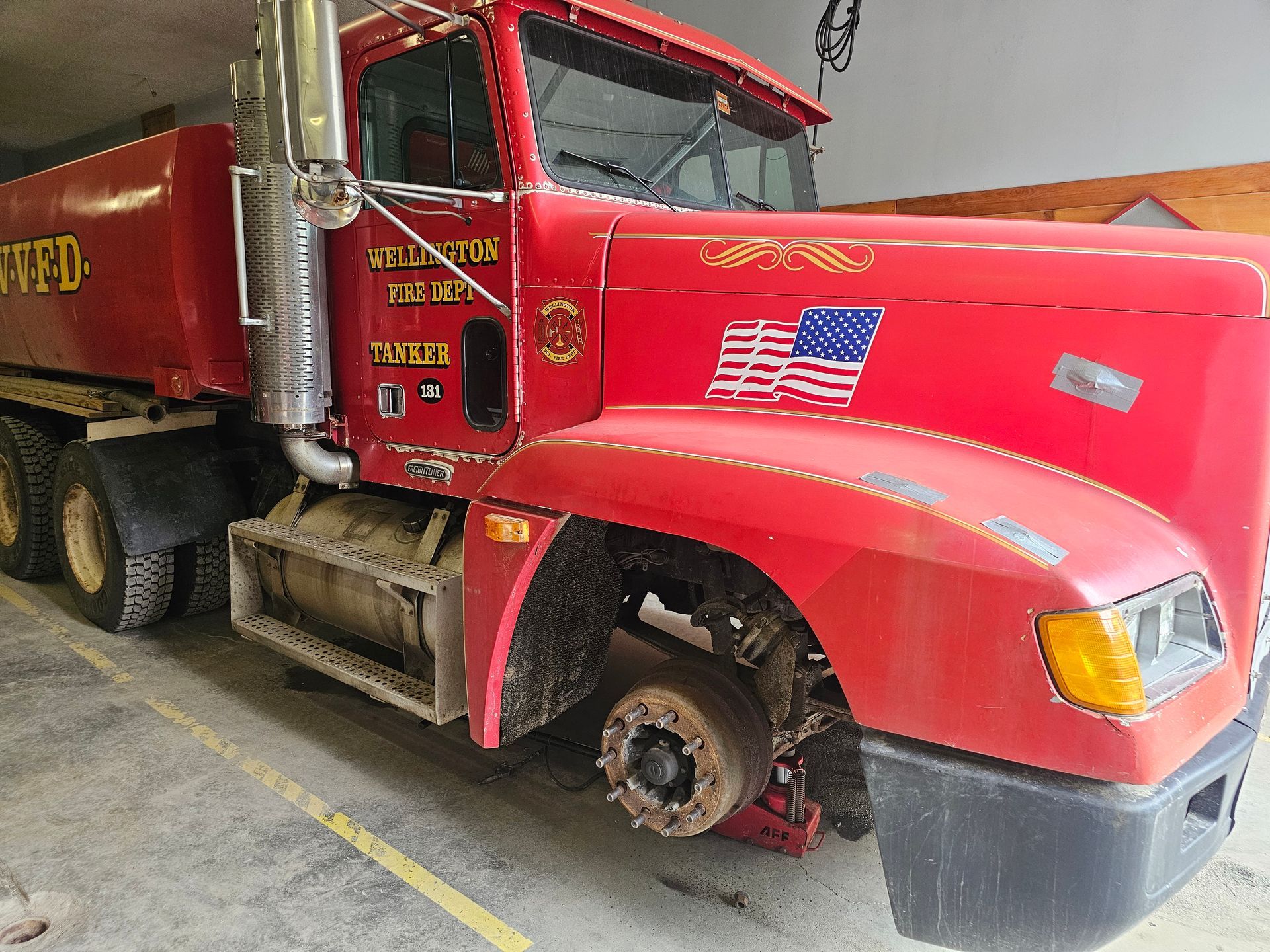 A red dump truck with an american flag on the front is parked in a garage.