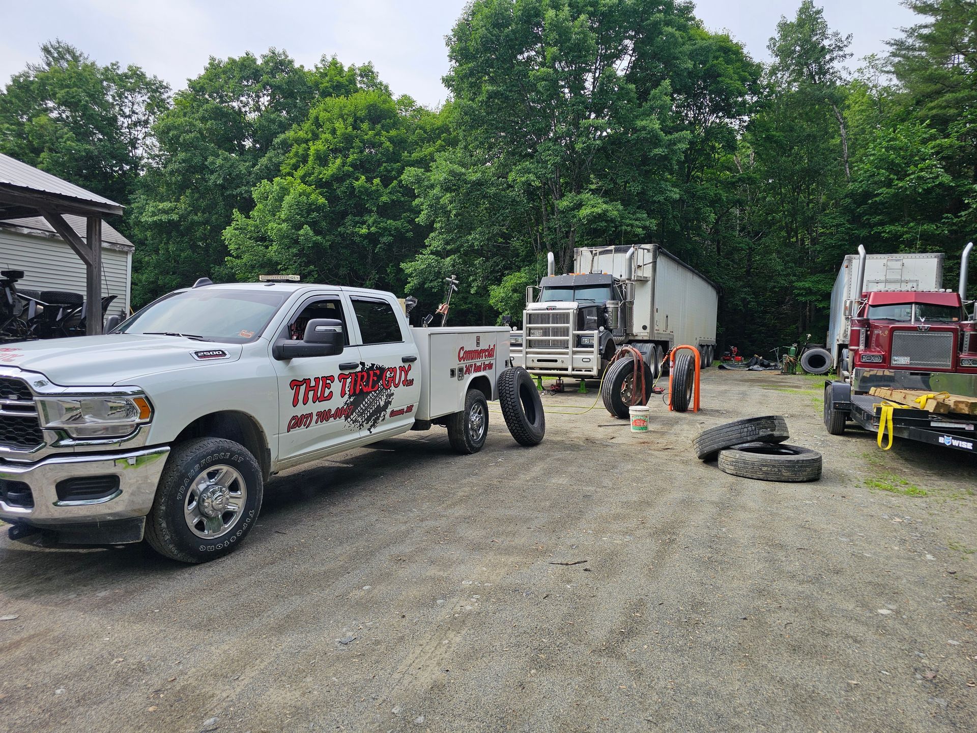 A tow truck is parked next to a semi truck in a dirt lot.
