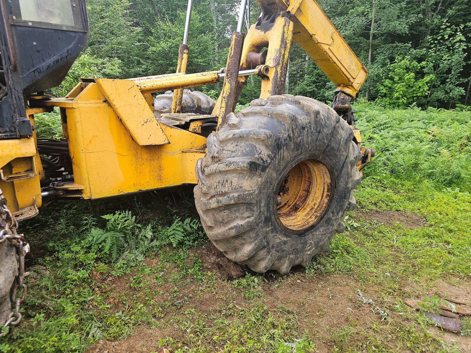 A yellow tractor with a large tire is sitting in the grass.