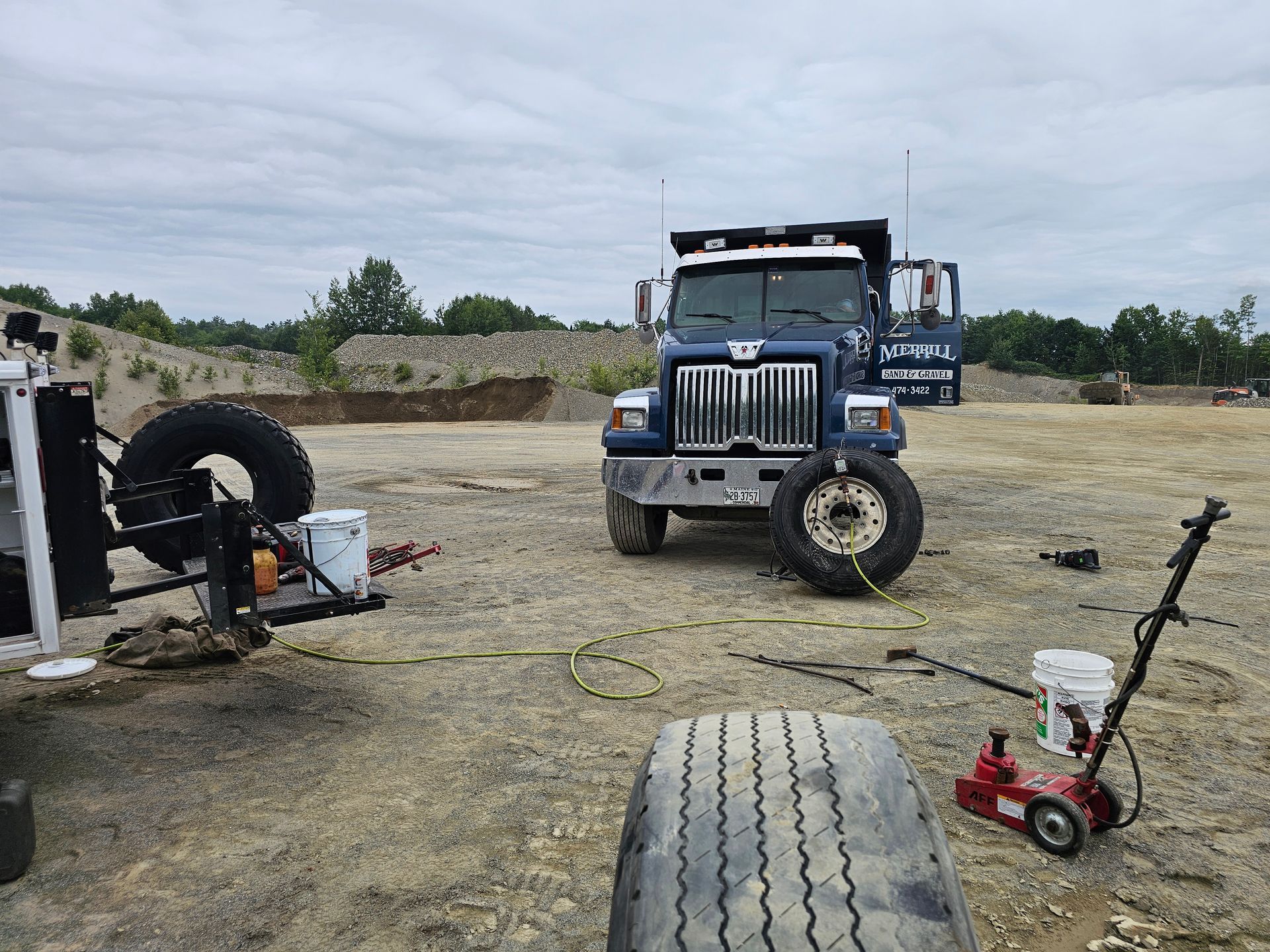 A truck with a flat tire is sitting in a dirt field.
