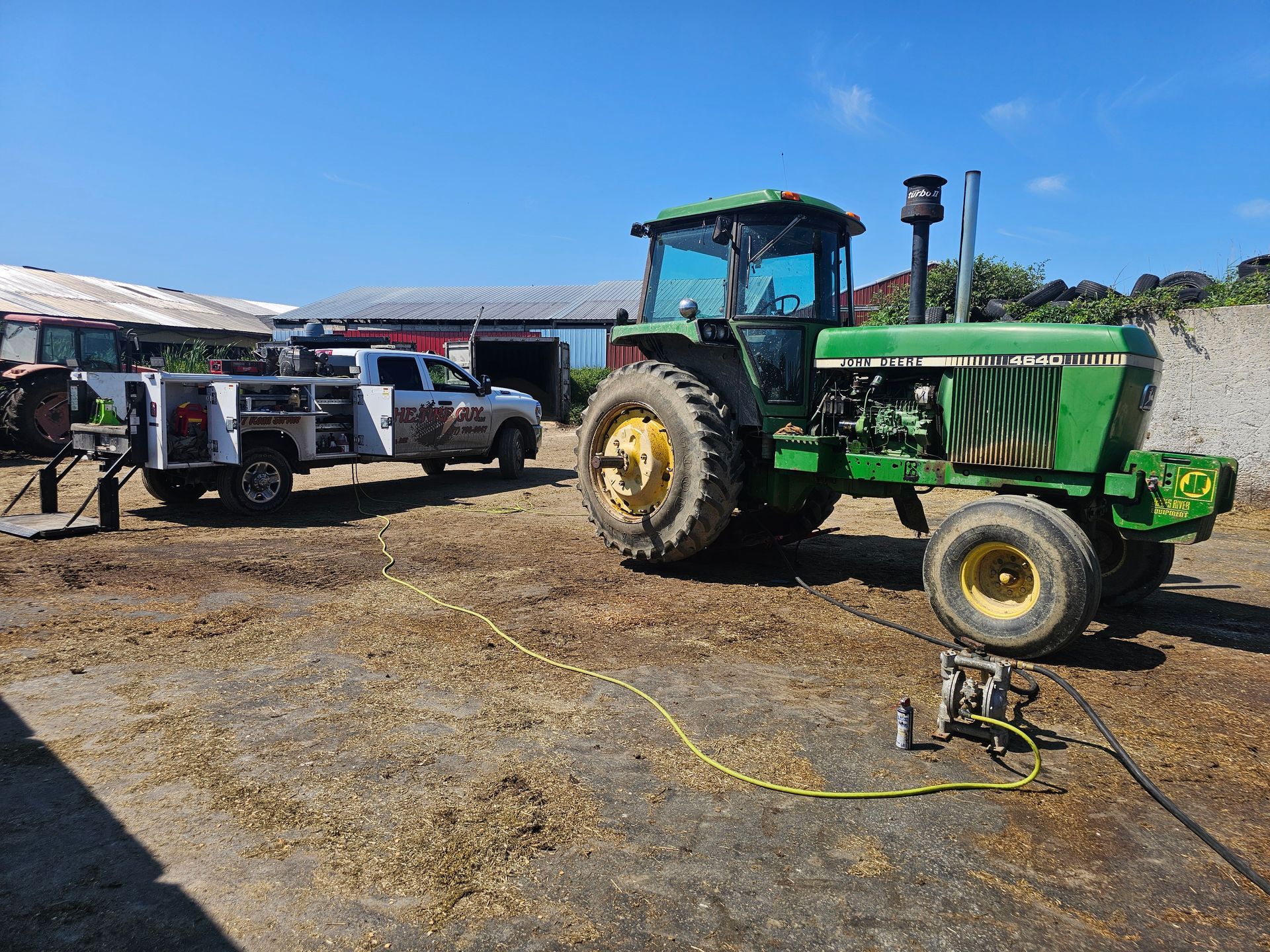 A green tractor is parked in a dirt field next to a white truck.