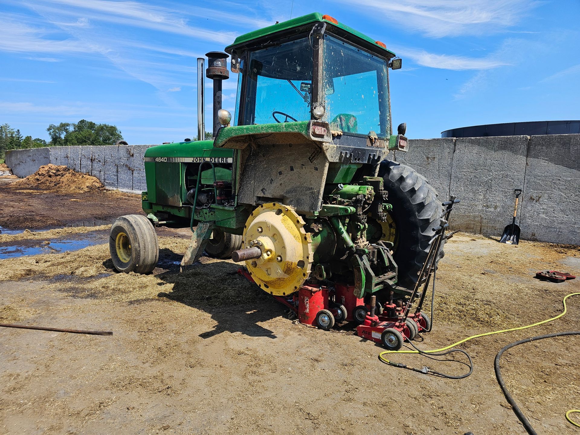 A green john deere tractor is sitting on a jack in the dirt.