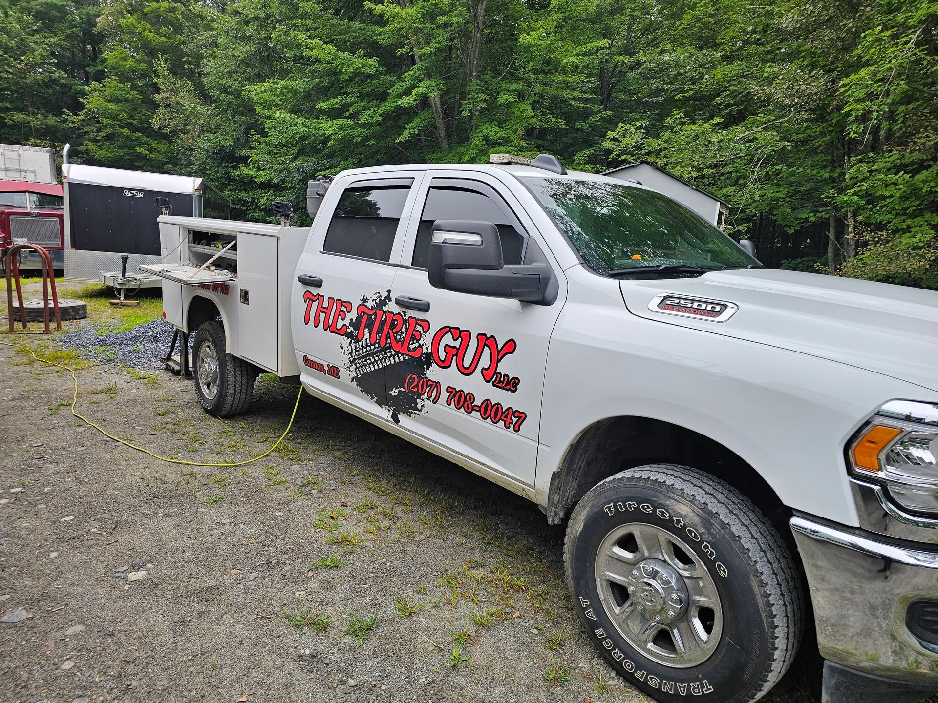 A white truck with a trailer attached to it is parked in a gravel lot.