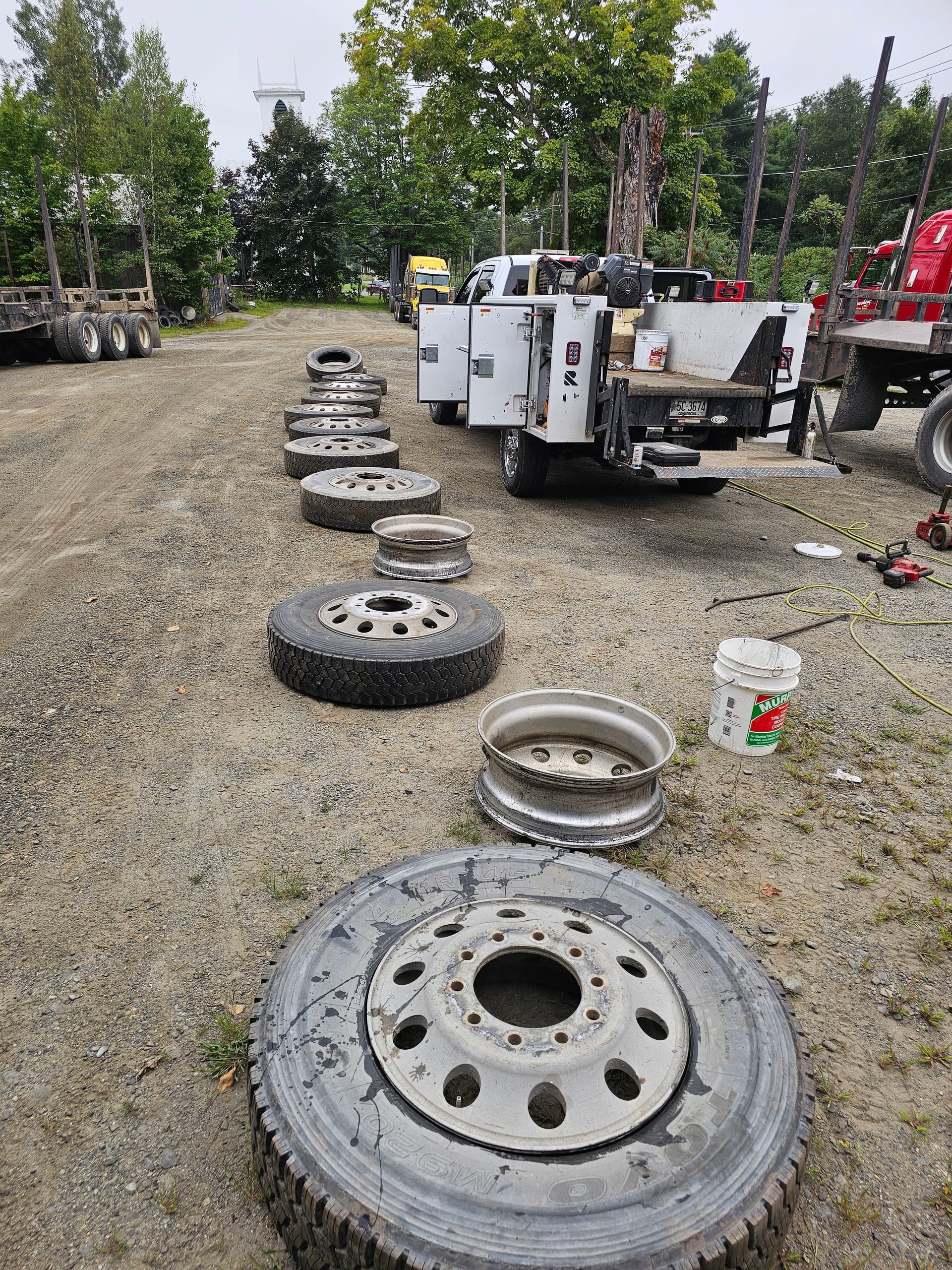 A row of tires and rims in a gravel lot next to a truck.