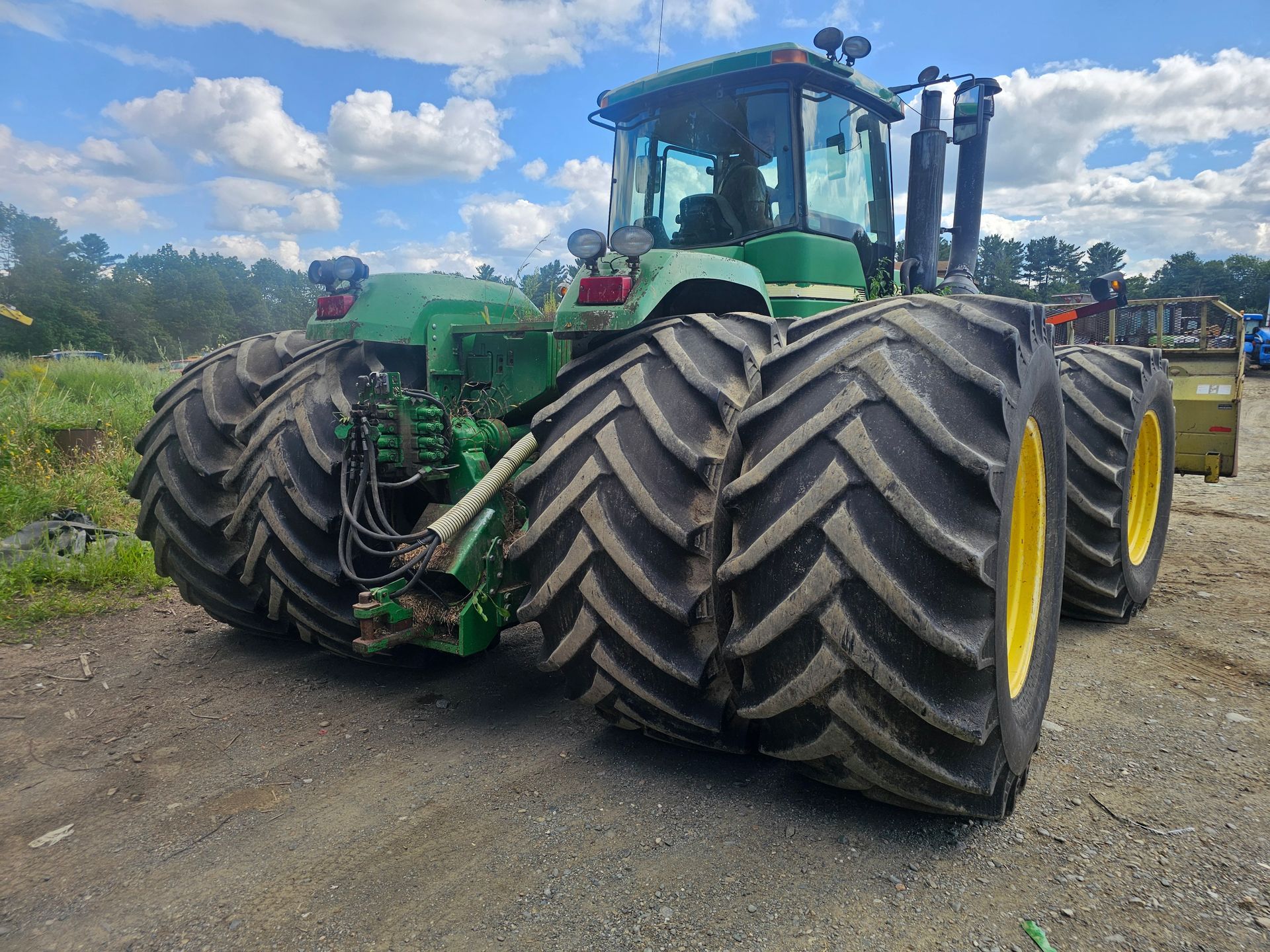A green john deere tractor with large tires is parked in a gravel lot.