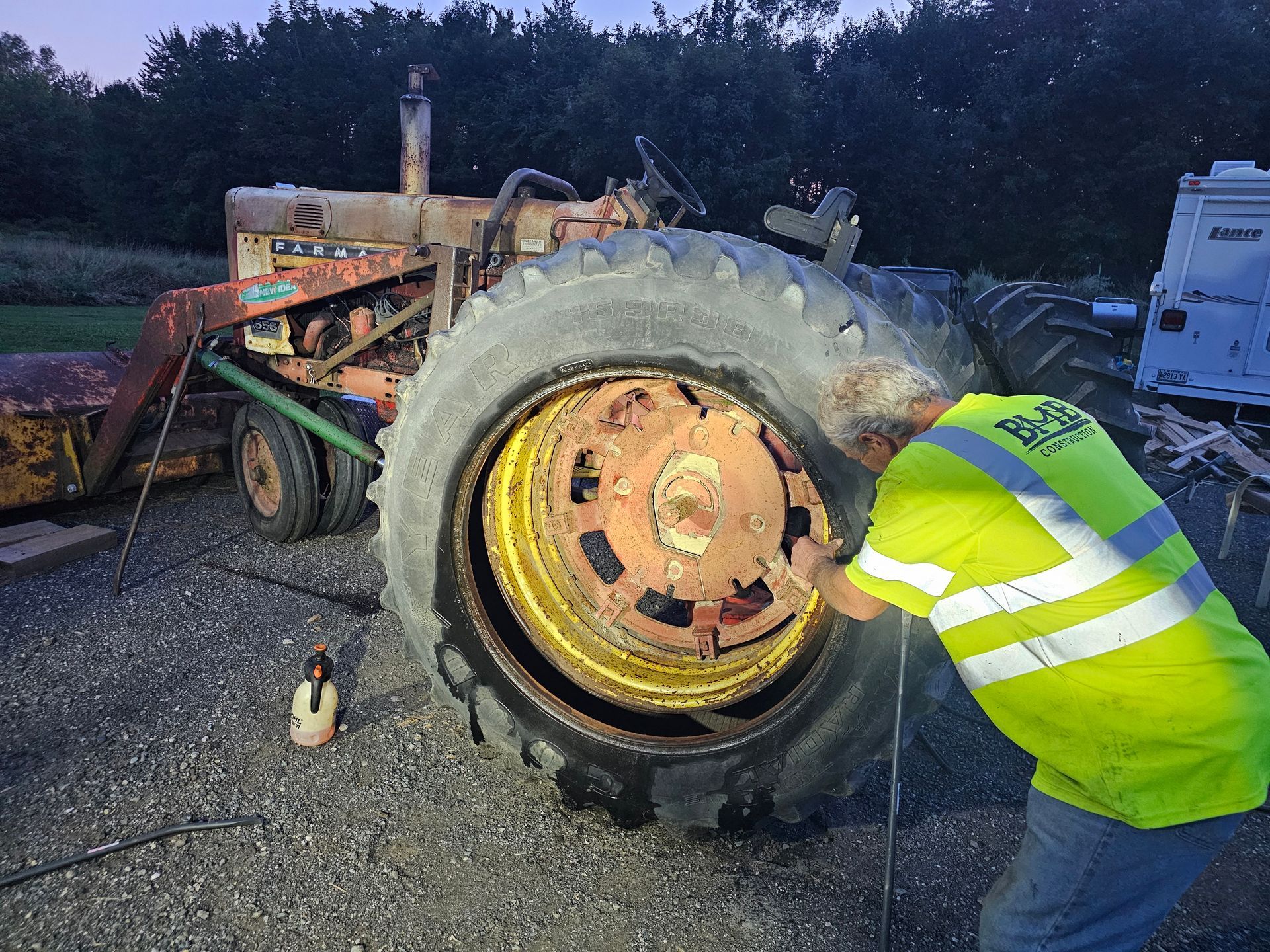 A man in a yellow vest is working on a tractor tire.