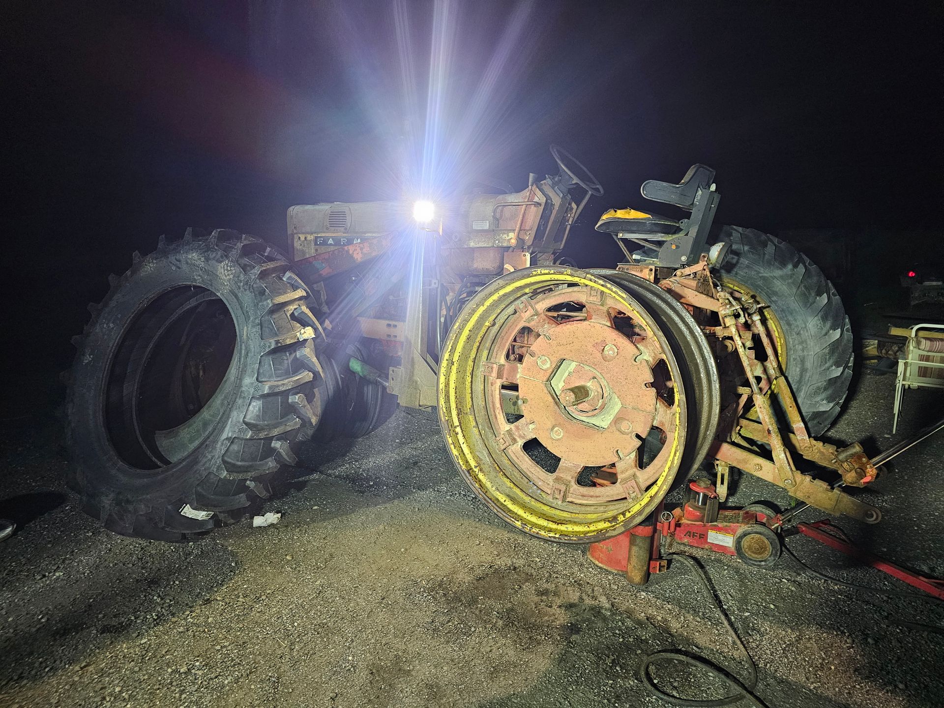 An old rusty tractor is sitting on a jack at night.