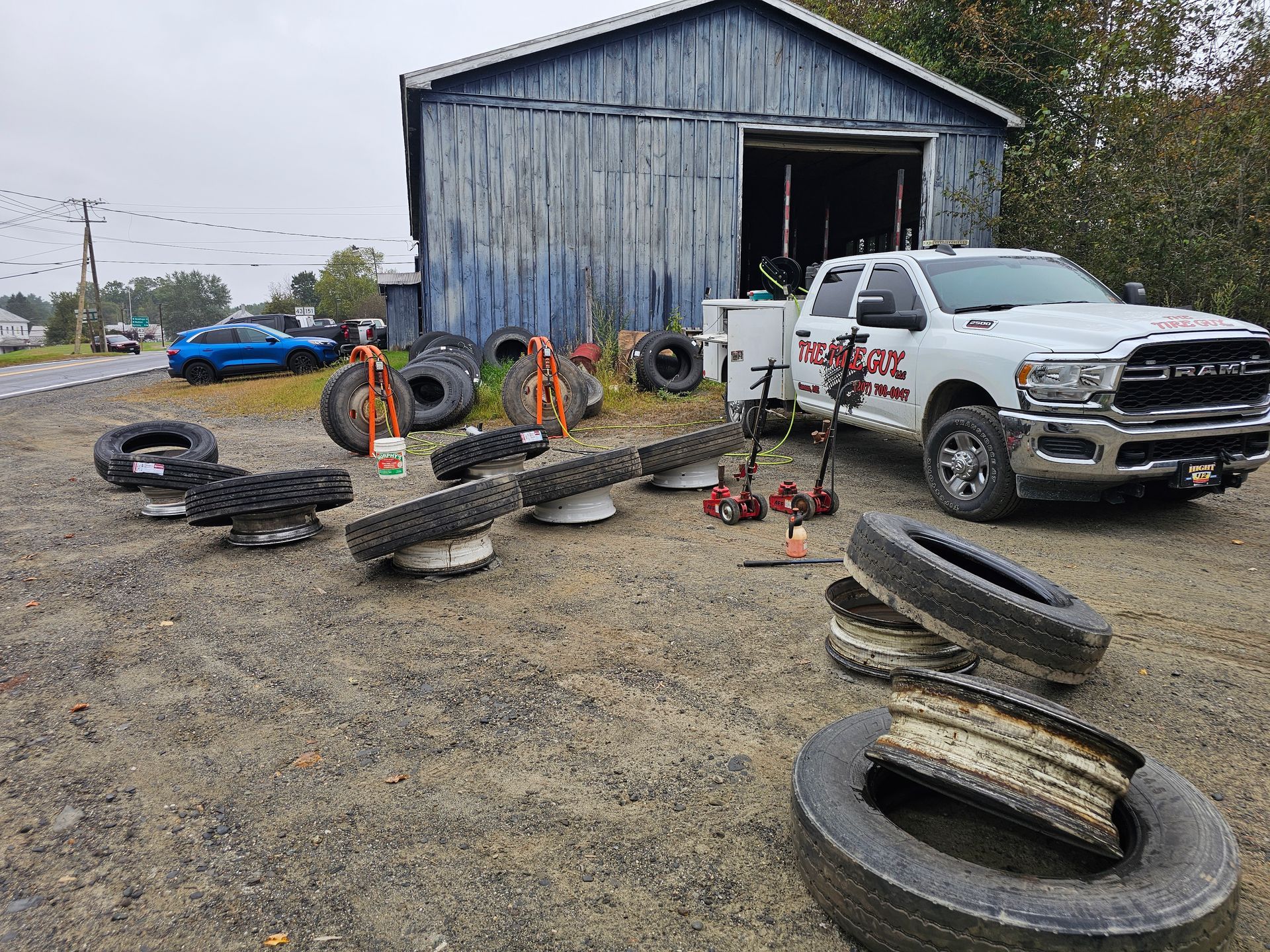 A white truck is parked in front of a blue barn surrounded by tires.