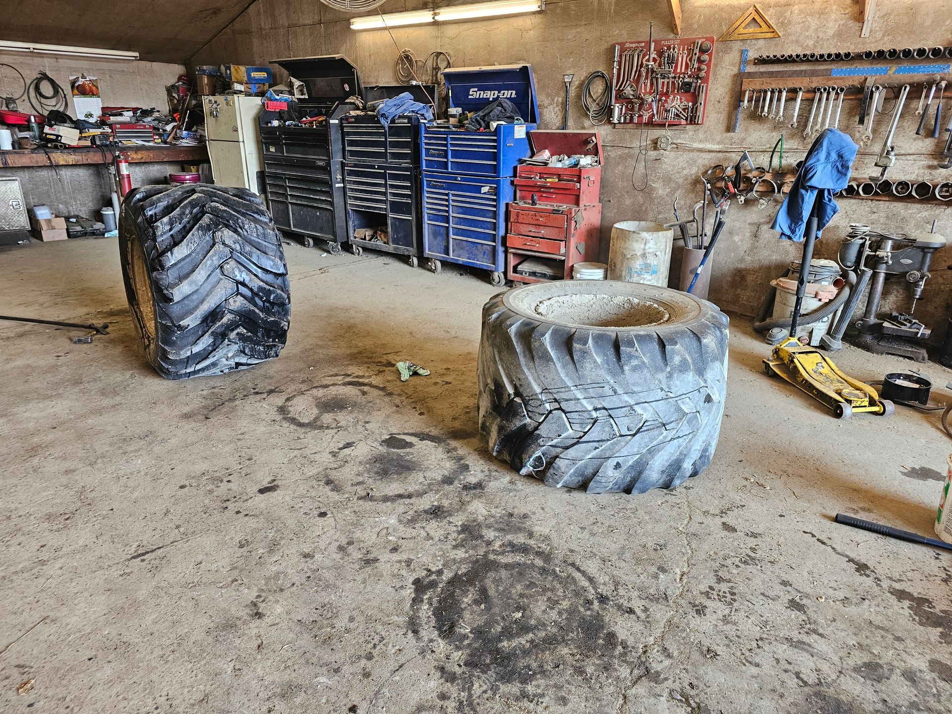 Two tires are sitting on the floor in a garage.