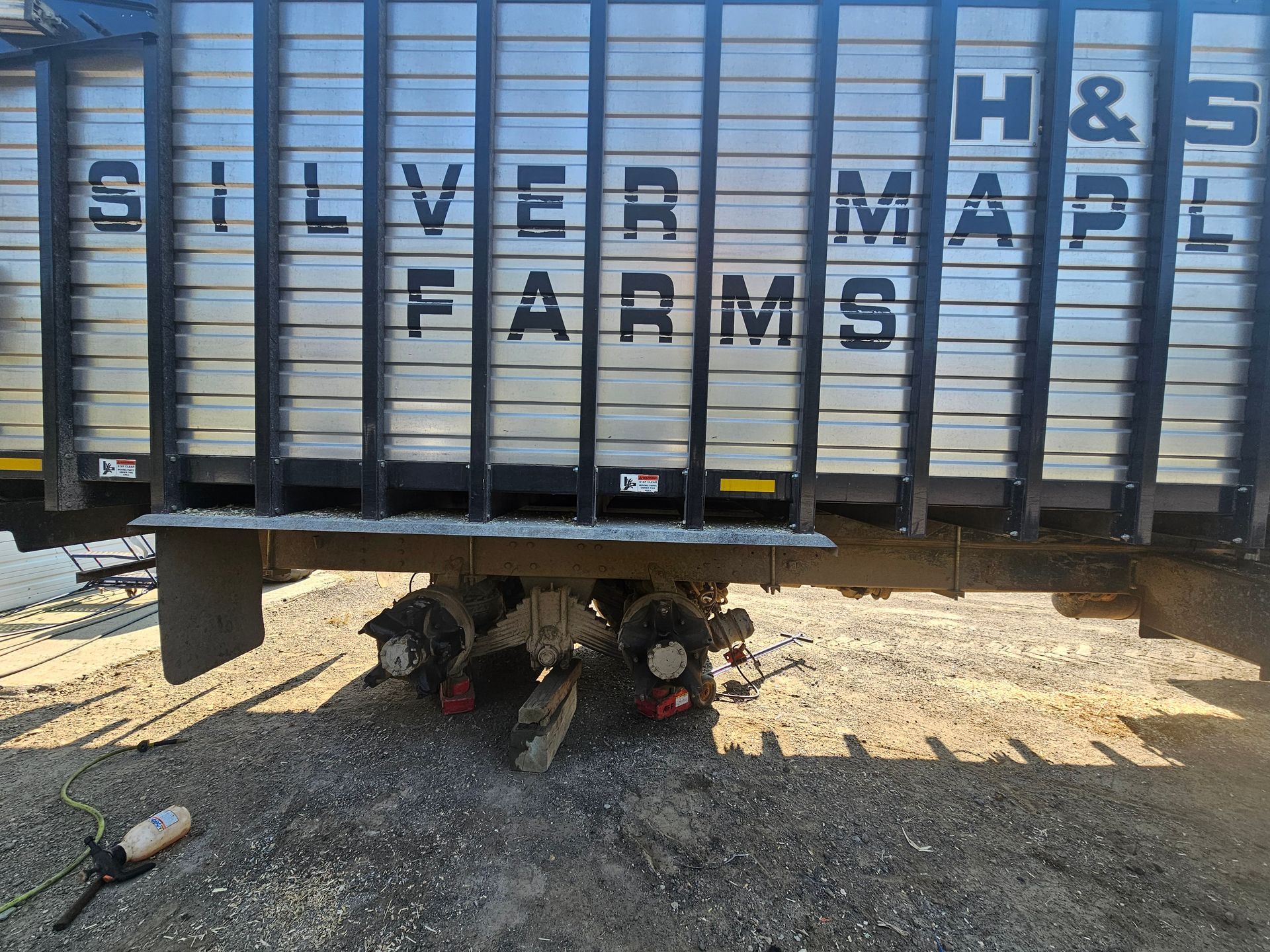 A silver farms trailer is parked in the dirt.