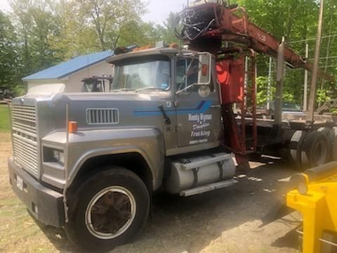 A large truck with a crane on the back is parked in a dirt lot.
