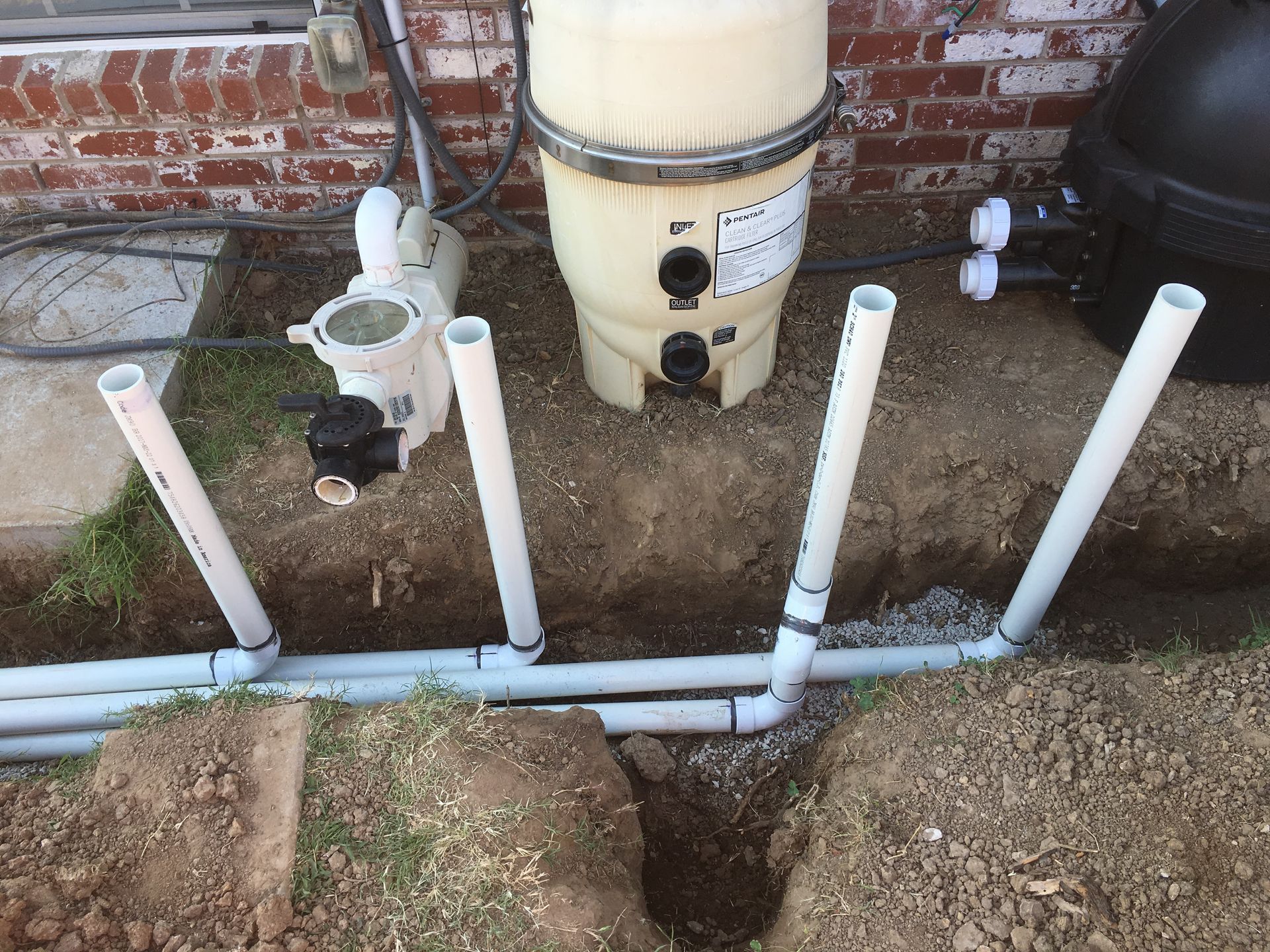 A swimming pool filter is sitting in the dirt next to a brick building.