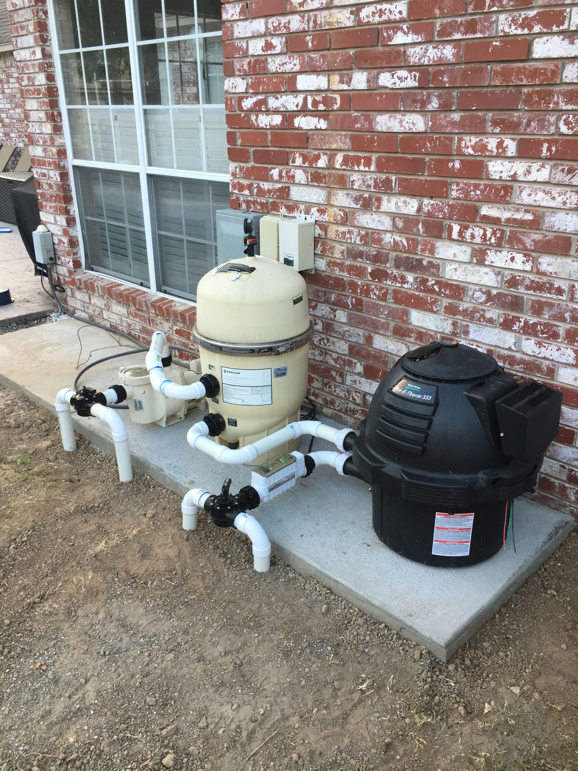 A swimming pool filter and heater are sitting on the side of a brick building.