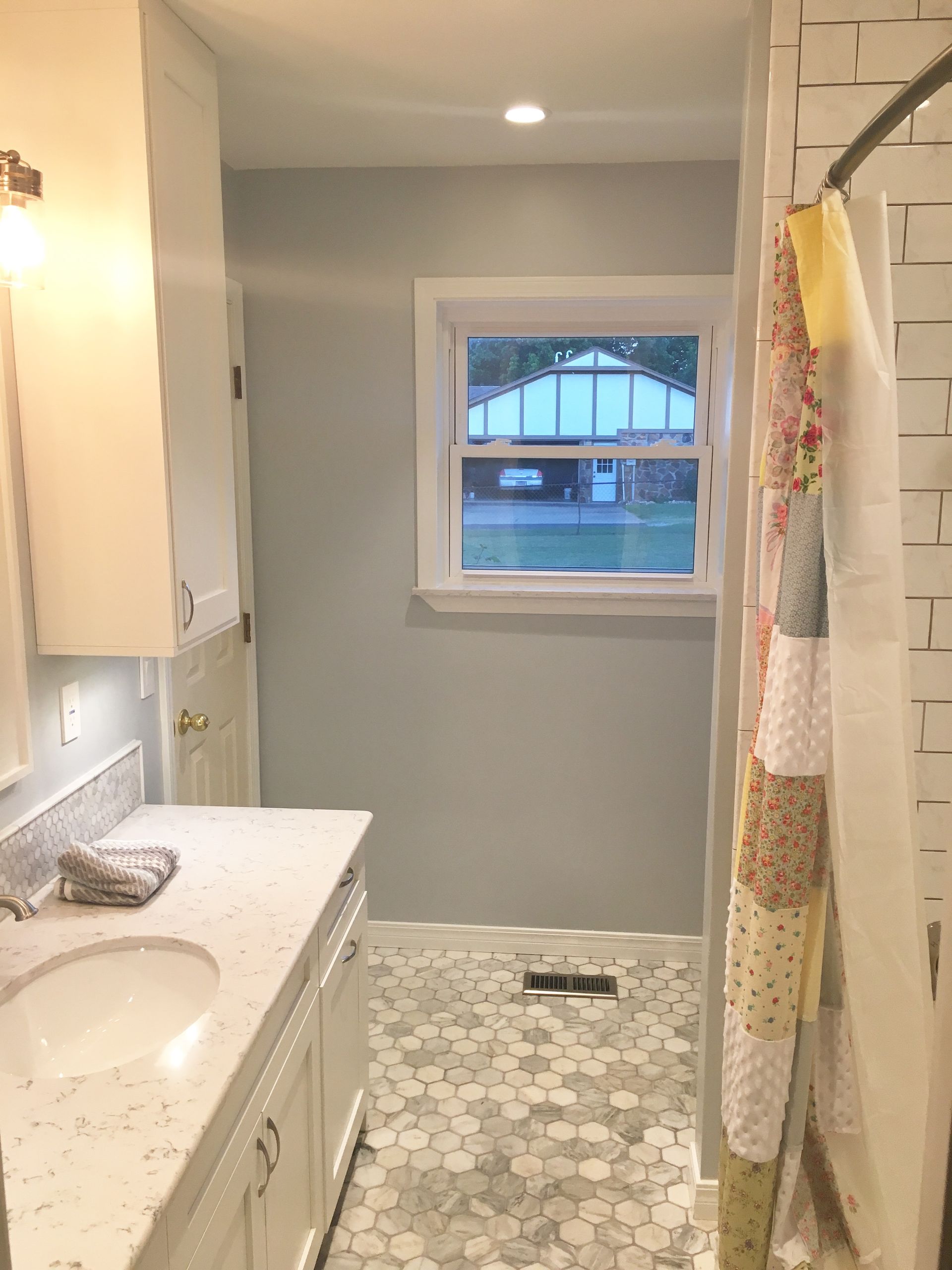 A bathroom with a sink , shower , and window.