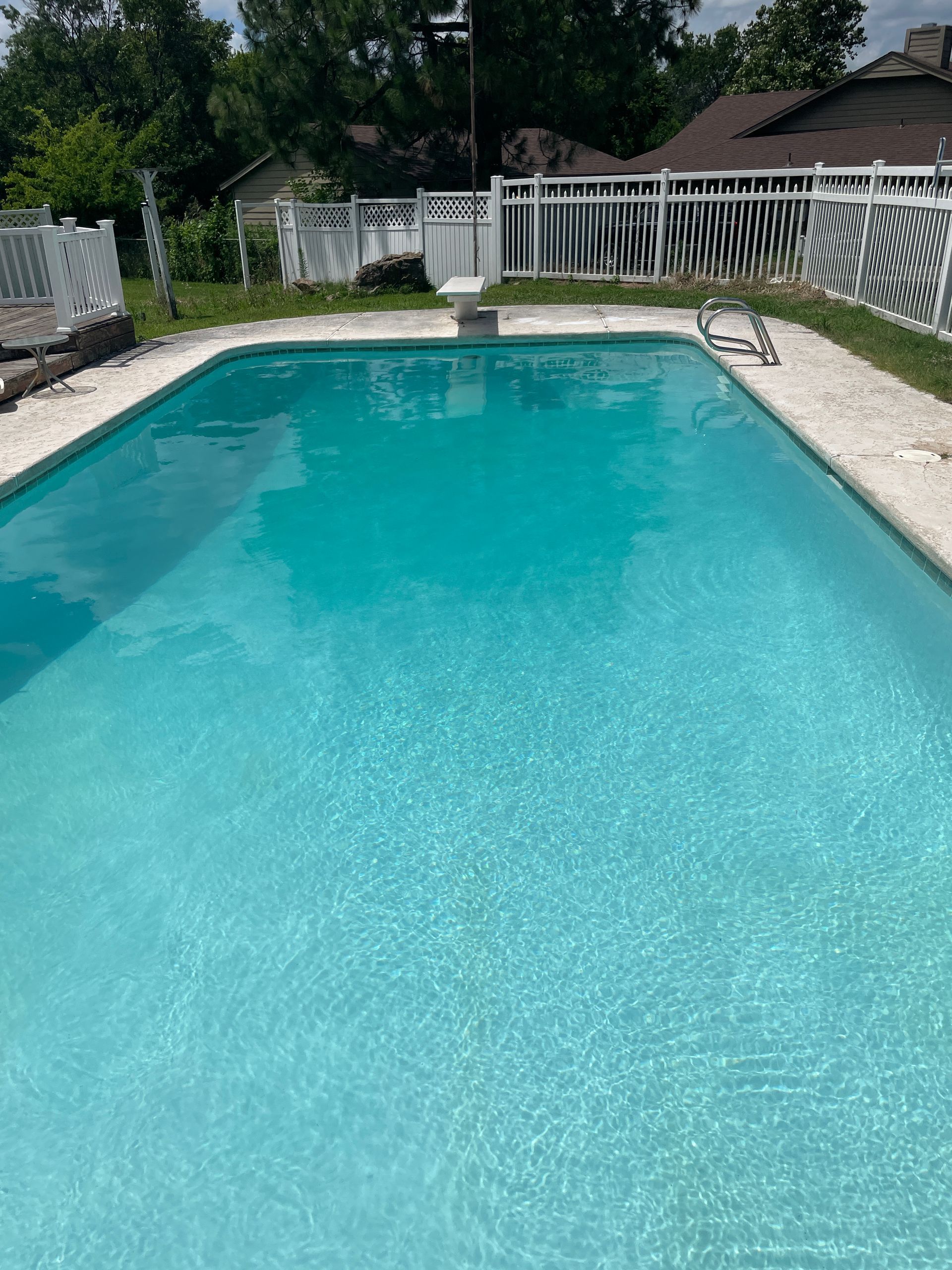 A large swimming pool with a white fence in the backyard.