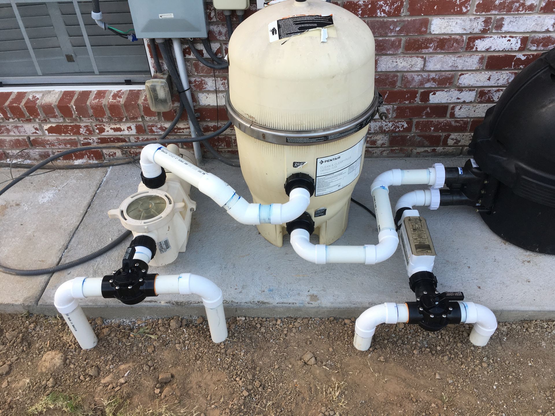 A swimming pool filter is sitting on a sidewalk next to a brick wall.