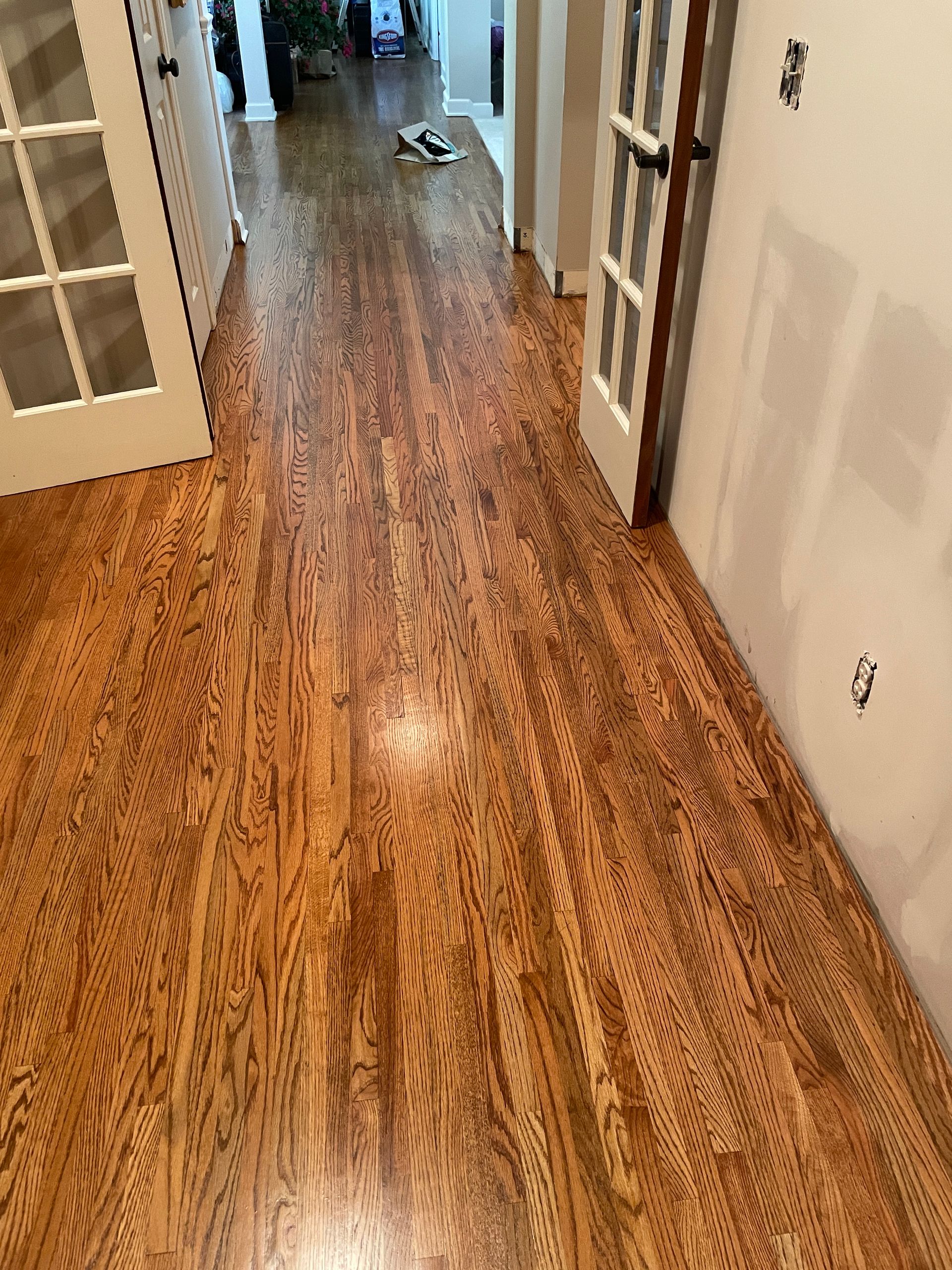 A hallway with hardwood floors and french doors in a house.