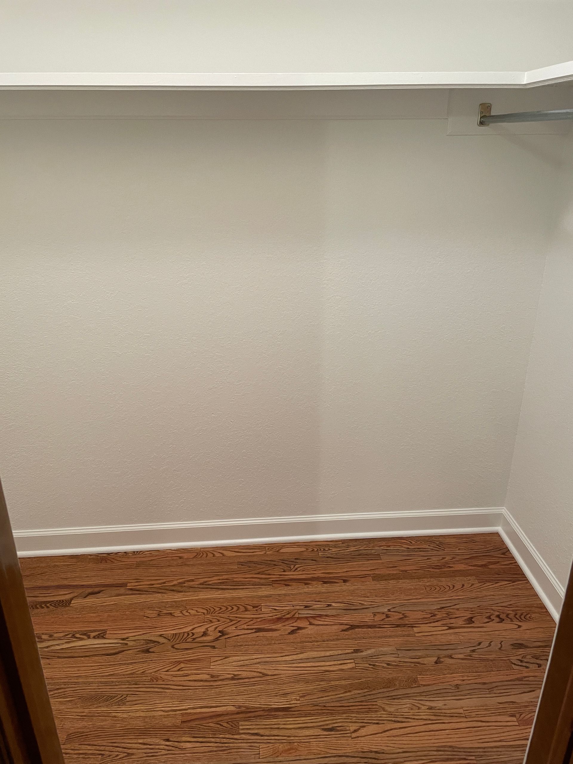 An empty walk in closet with hardwood floors and white walls.