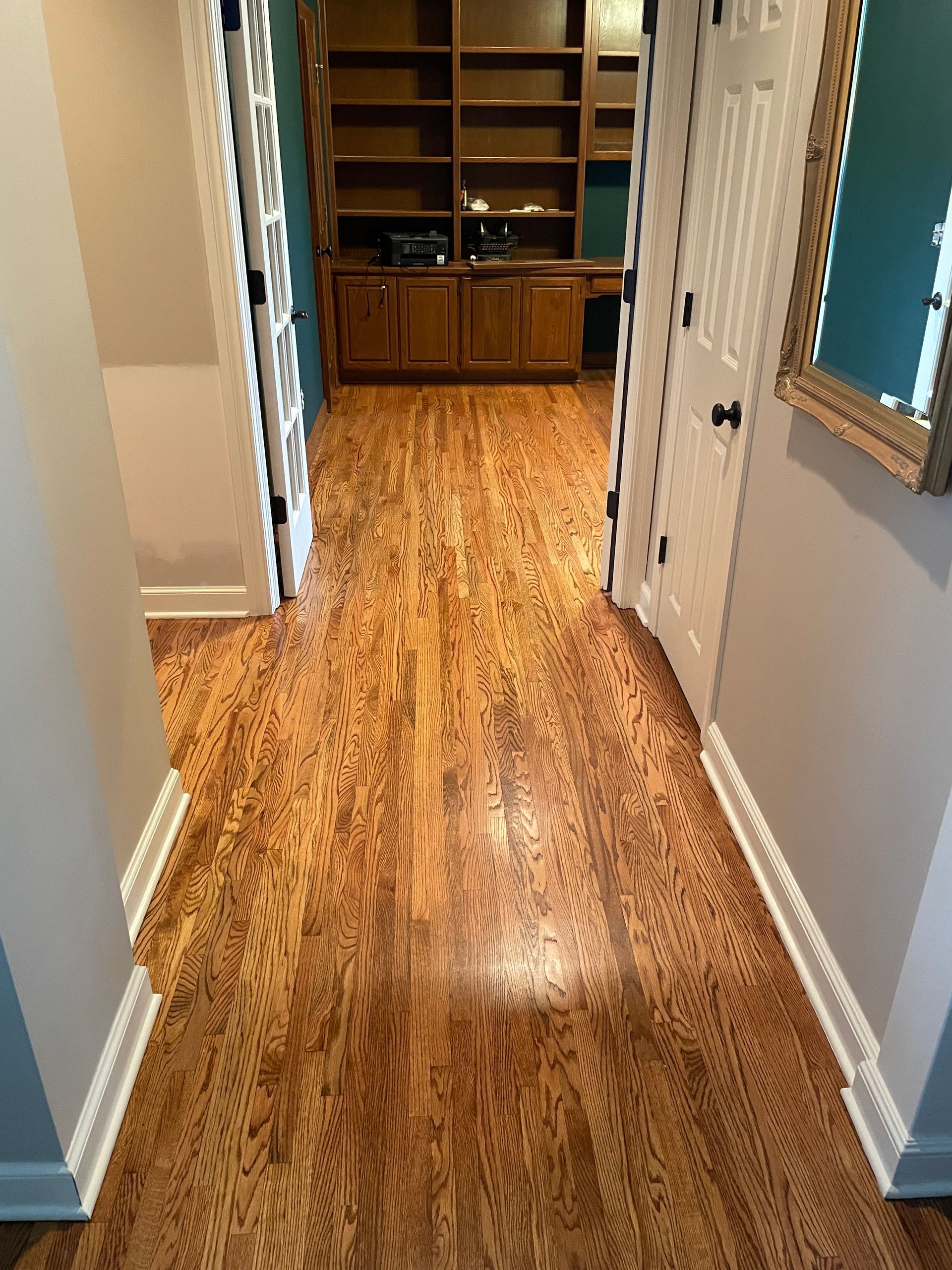 A hallway with hardwood floors and a mirror in a house.