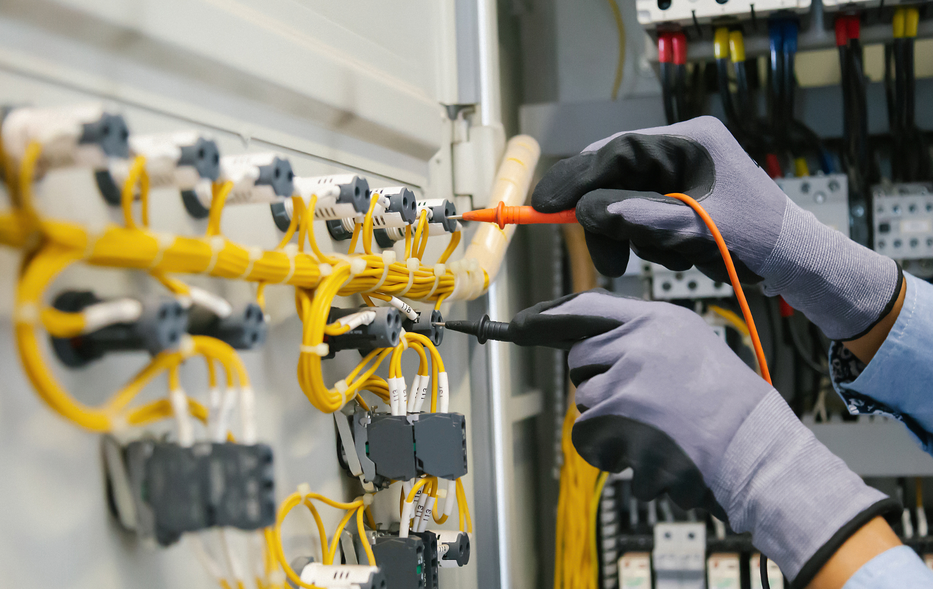 An electrician is working on an electrical panel with a multimeter.