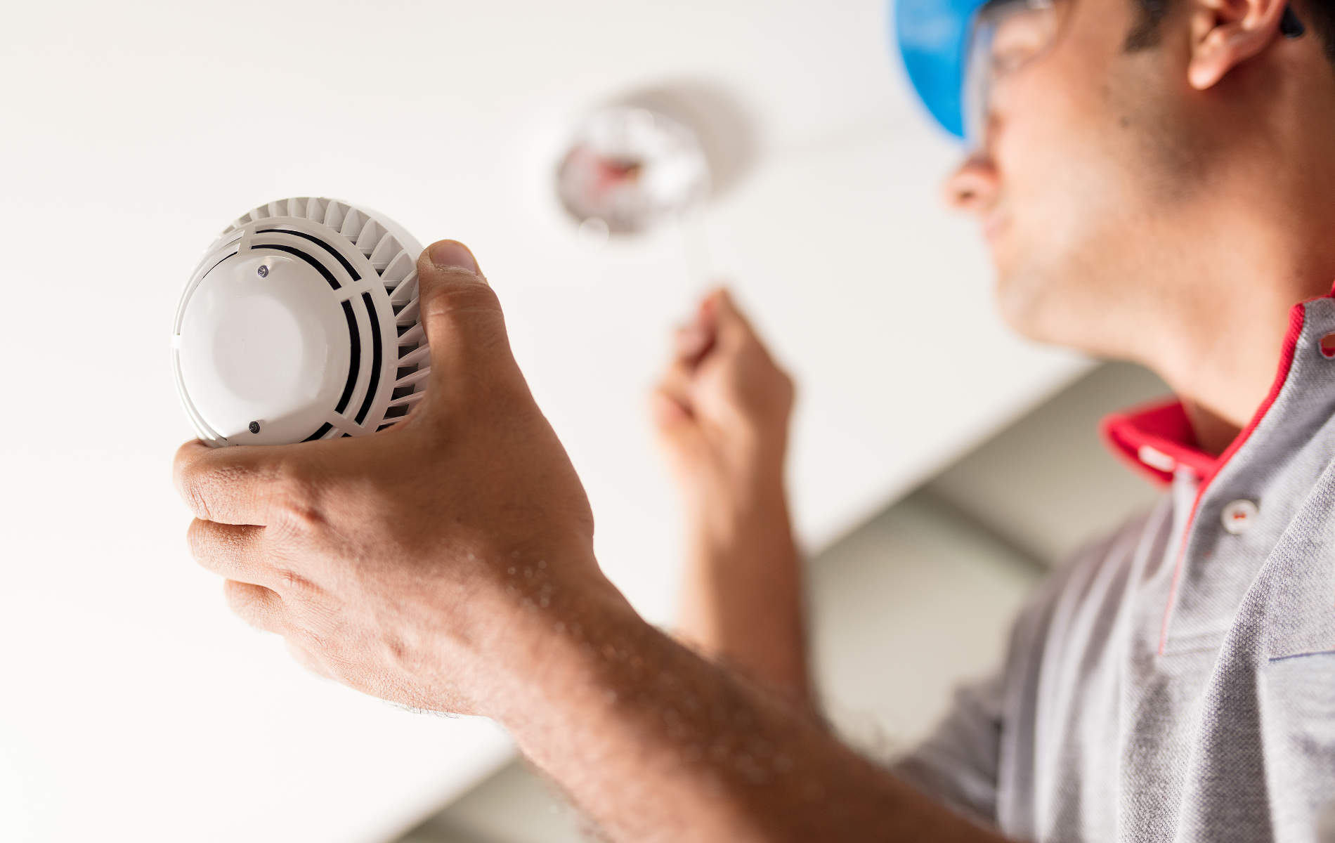 A man is holding a smoke detector in his hand.