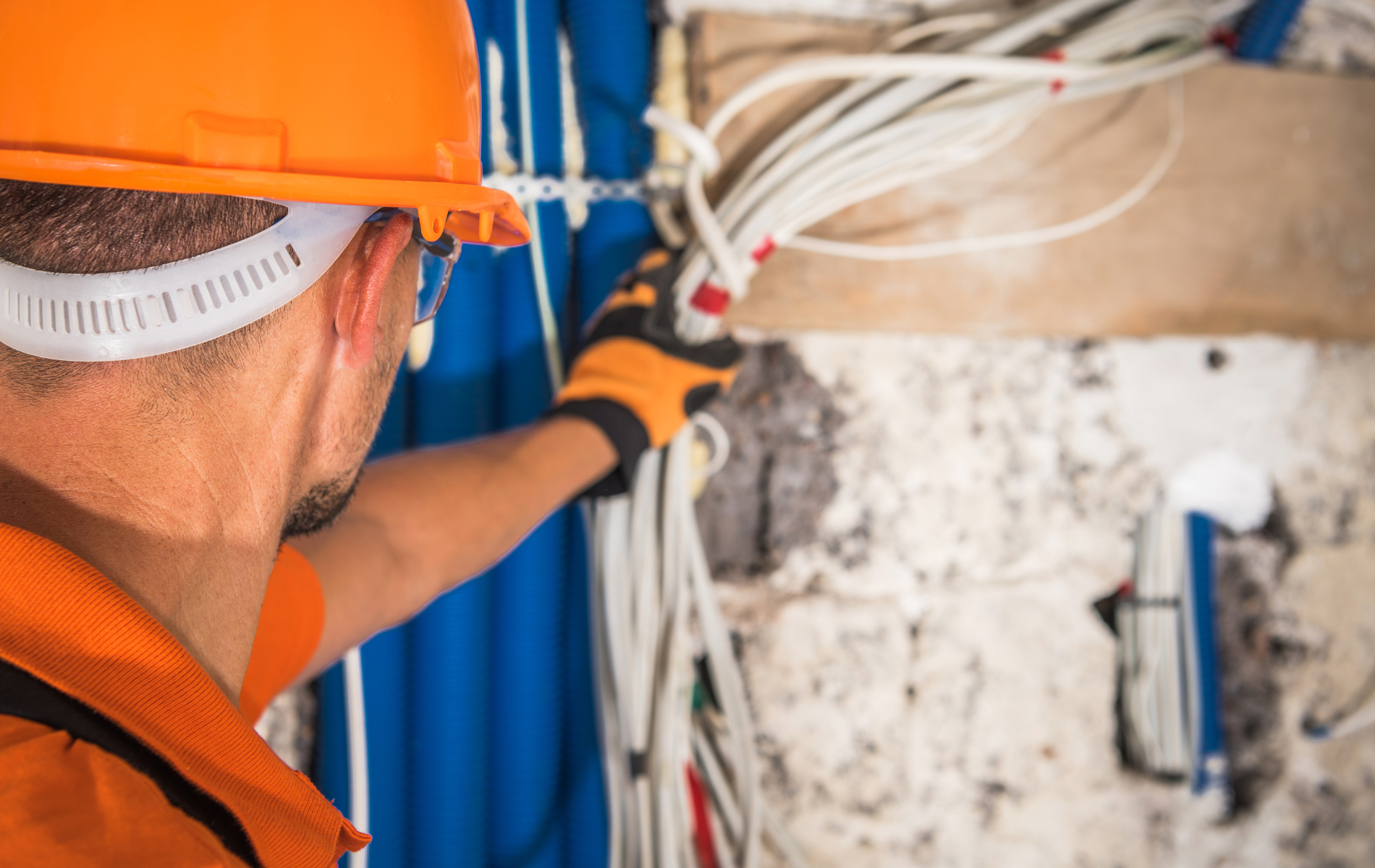 A man wearing a hard hat and gloves is working on electrical wires.