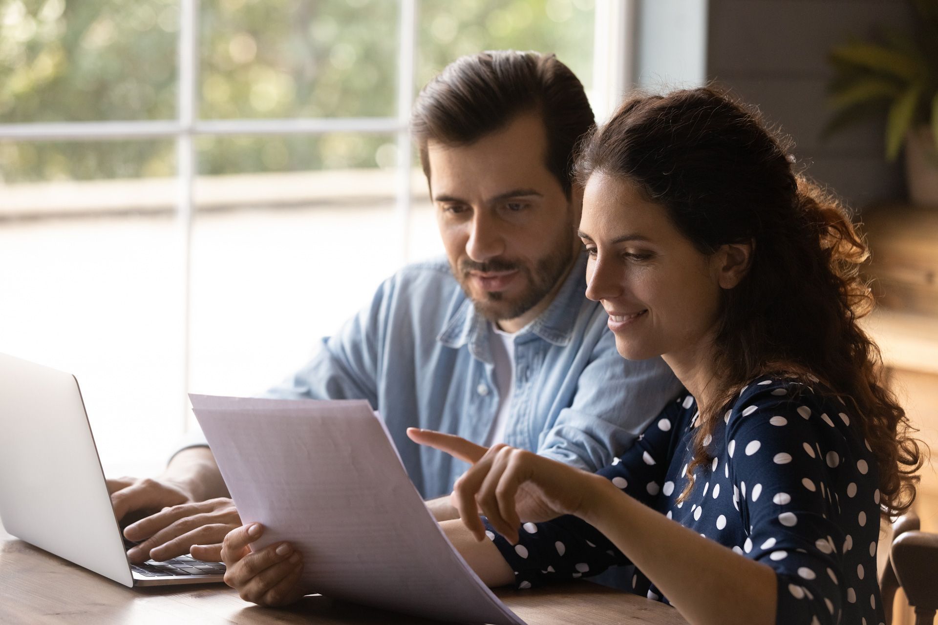 A man and a woman are sitting at a table looking at a laptop.