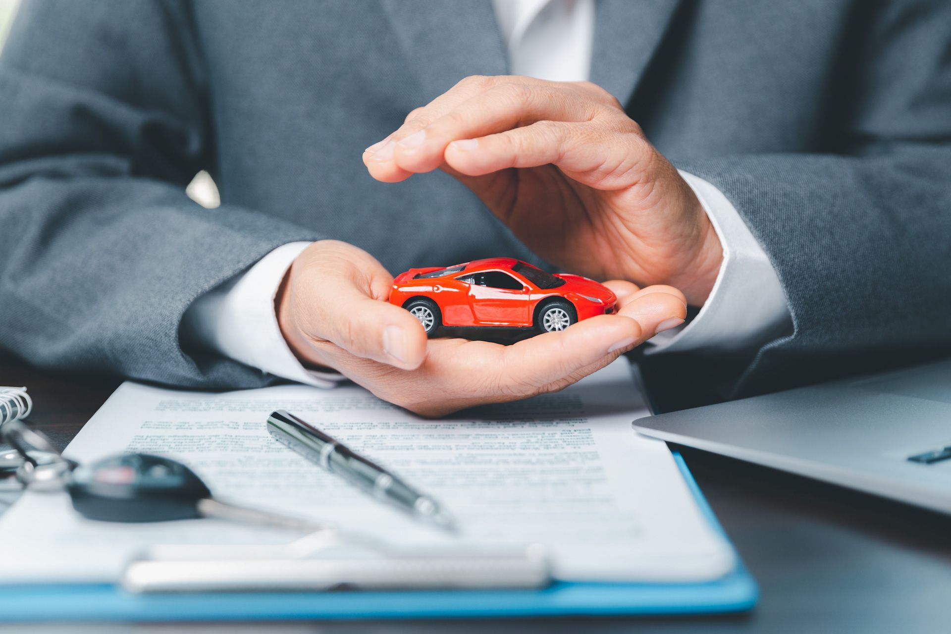 A man in a suit is holding a red toy car in his hands.