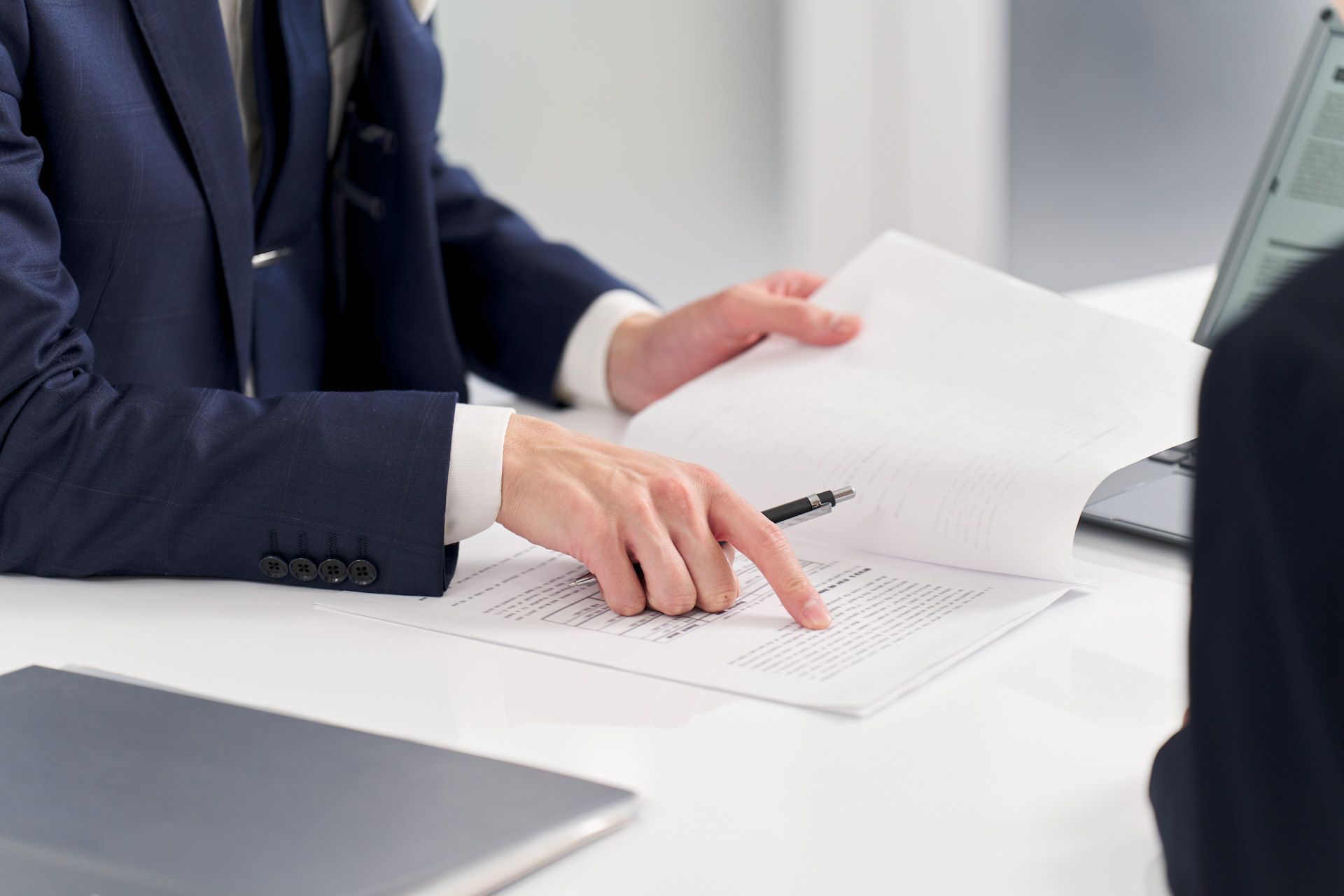 A man in a suit is sitting at a table looking at a piece of paper.