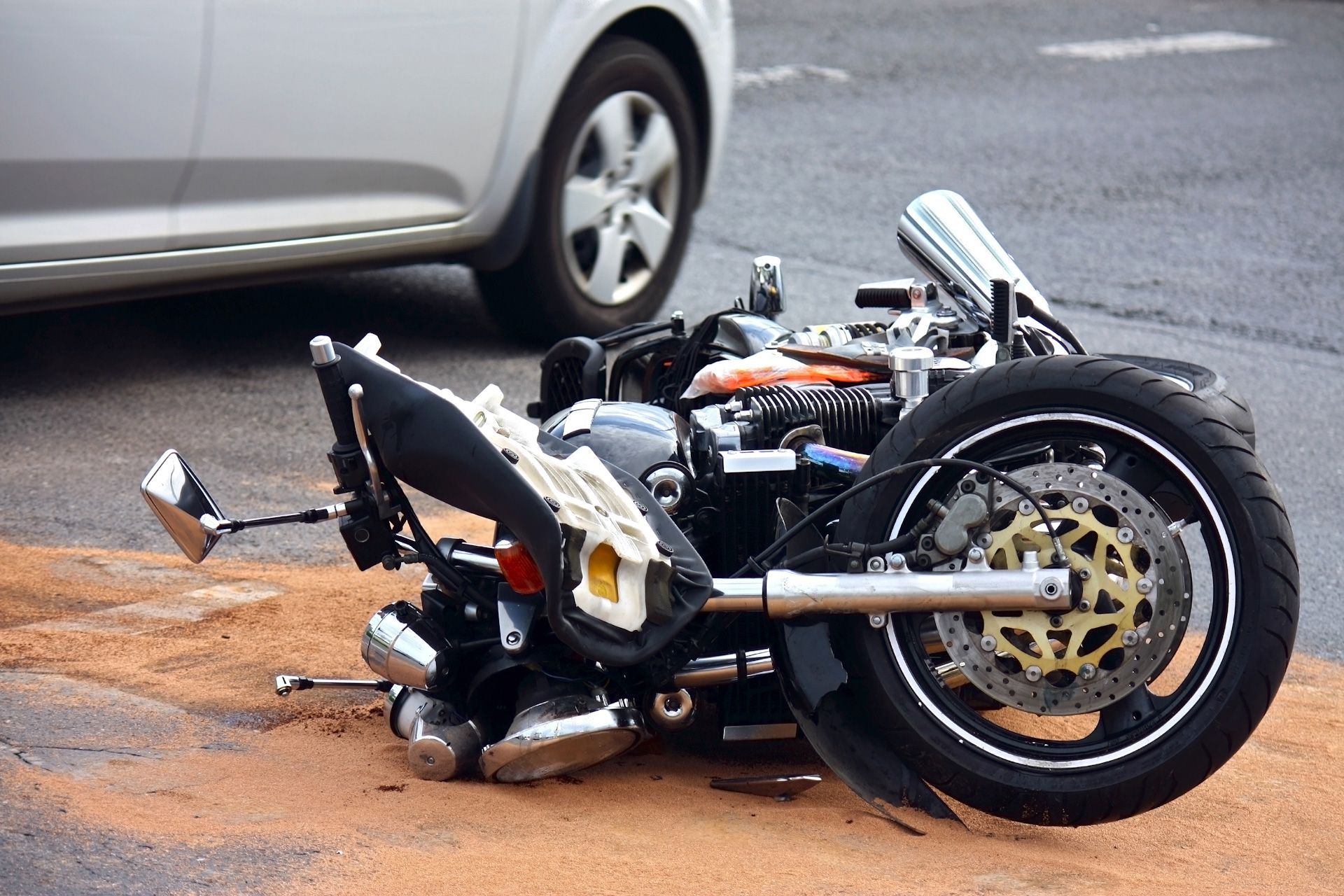 A motorcycle has crashed into a car on the side of the road.