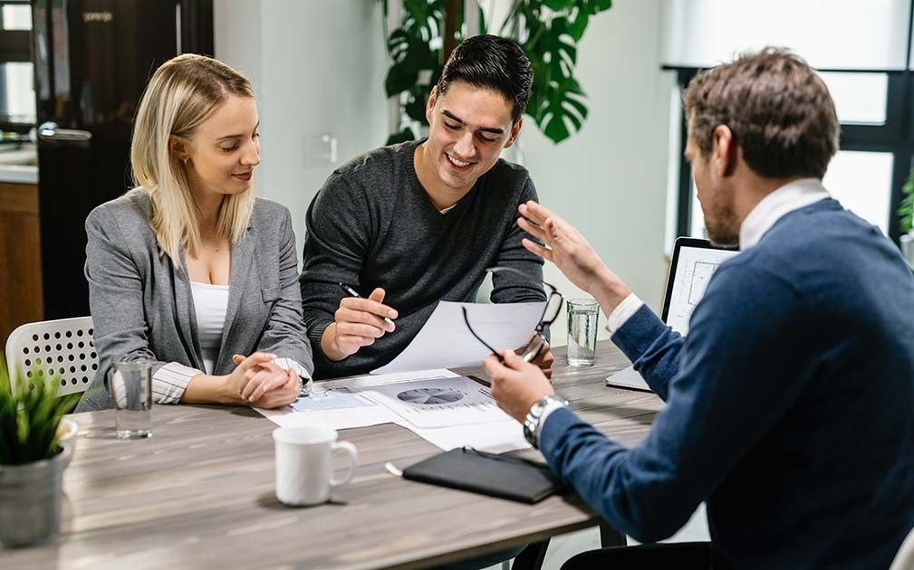 A man and a woman are sitting at a table talking to a man.