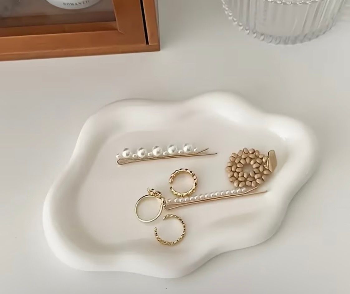 Gold jewelry laid on a white wavy tray beside a small pearl hair clip and beaded ring holder