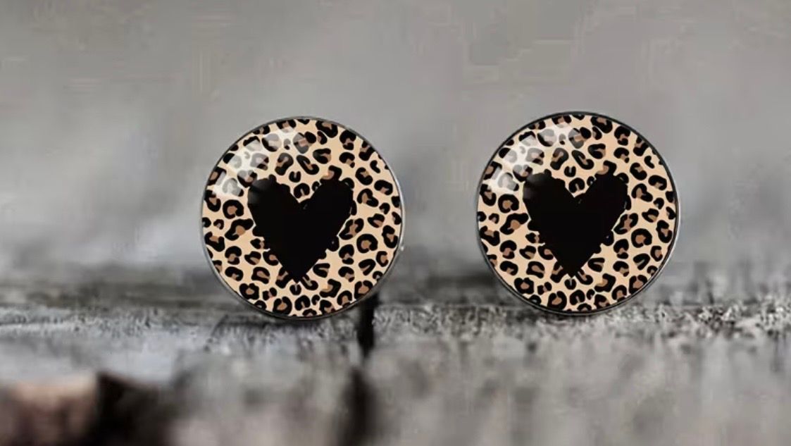 Two leopard-print heart stud earrings on a gray surface.