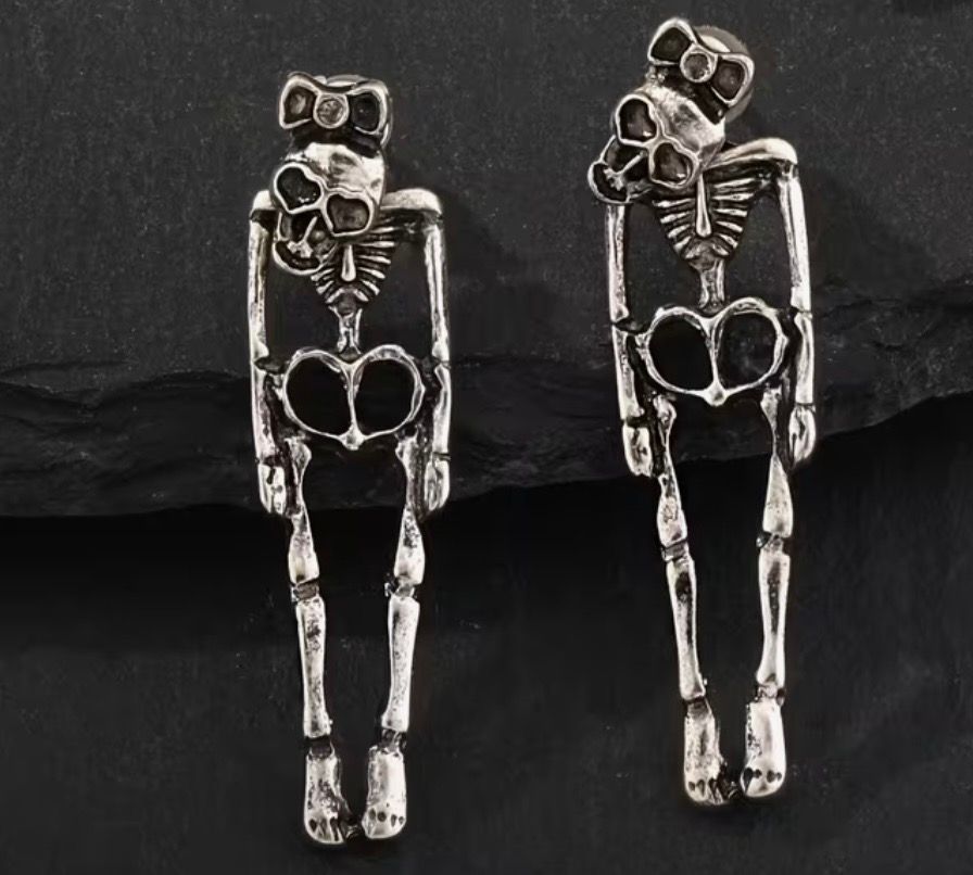 Pair of silver skeleton-shaped earrings on a black background