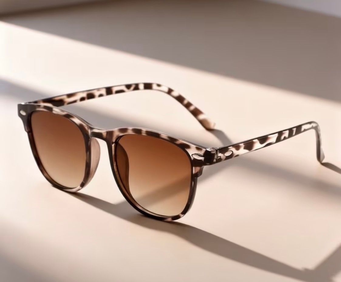Leopard-print sunglasses with brown lenses on a light surface in soft sunlight