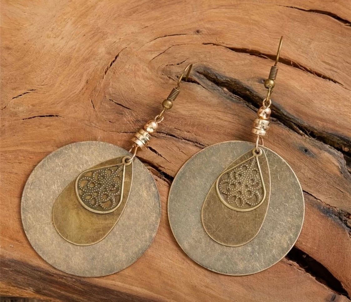 Pair of gold-tone earrings with circular pendants on a wooden surface