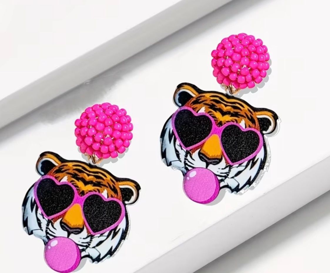 Two tiger-face earrings with pink heart sunglasses and pom-pom studs on a white background