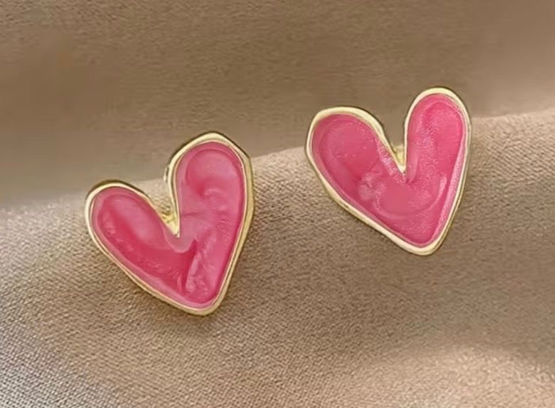 Two pink heart-shaped earrings with white outlines on a beige background