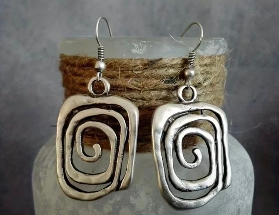 Twisted metal spiral earrings, one silver and one bronze, hanging against a twine-wrapped vase