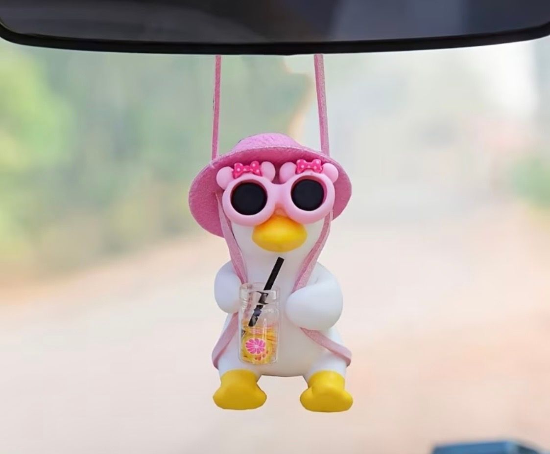Pink plush penguin charm with heart-shaped sunglasses hanging in a car