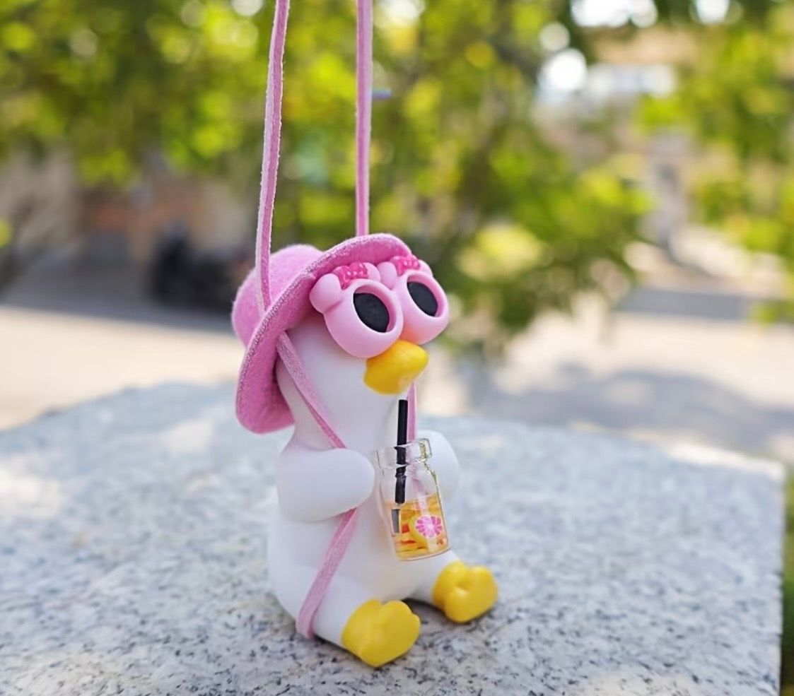 Pink plush penguin charm with heart-shaped sunglasses hanging in a car