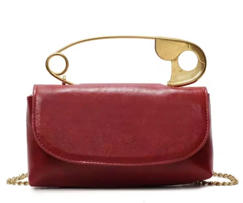 Red leather handbag with a gold safety-pin clasp and chain strap on a white background