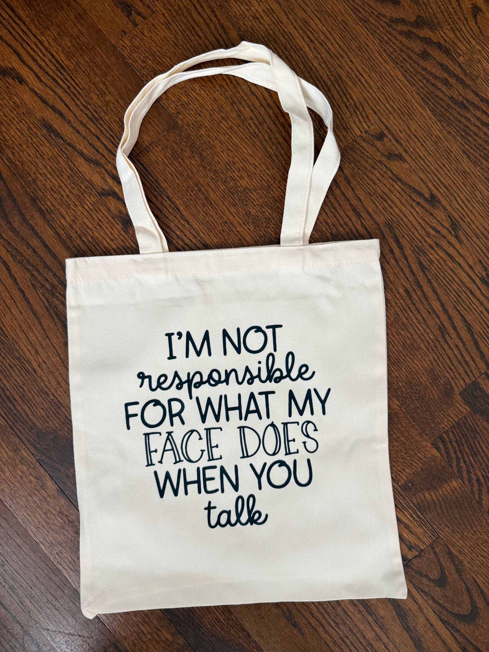 White tote bag on a wooden floor with the text, “I’m not responsible for what my face does when you talk.”