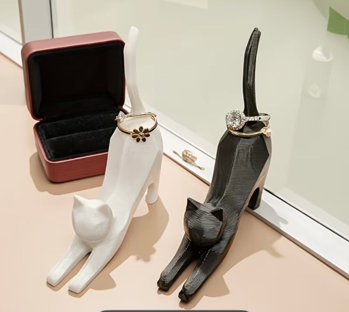 Two cat-shaped ring holders, one white and one black, with rings beside an open jewelry box