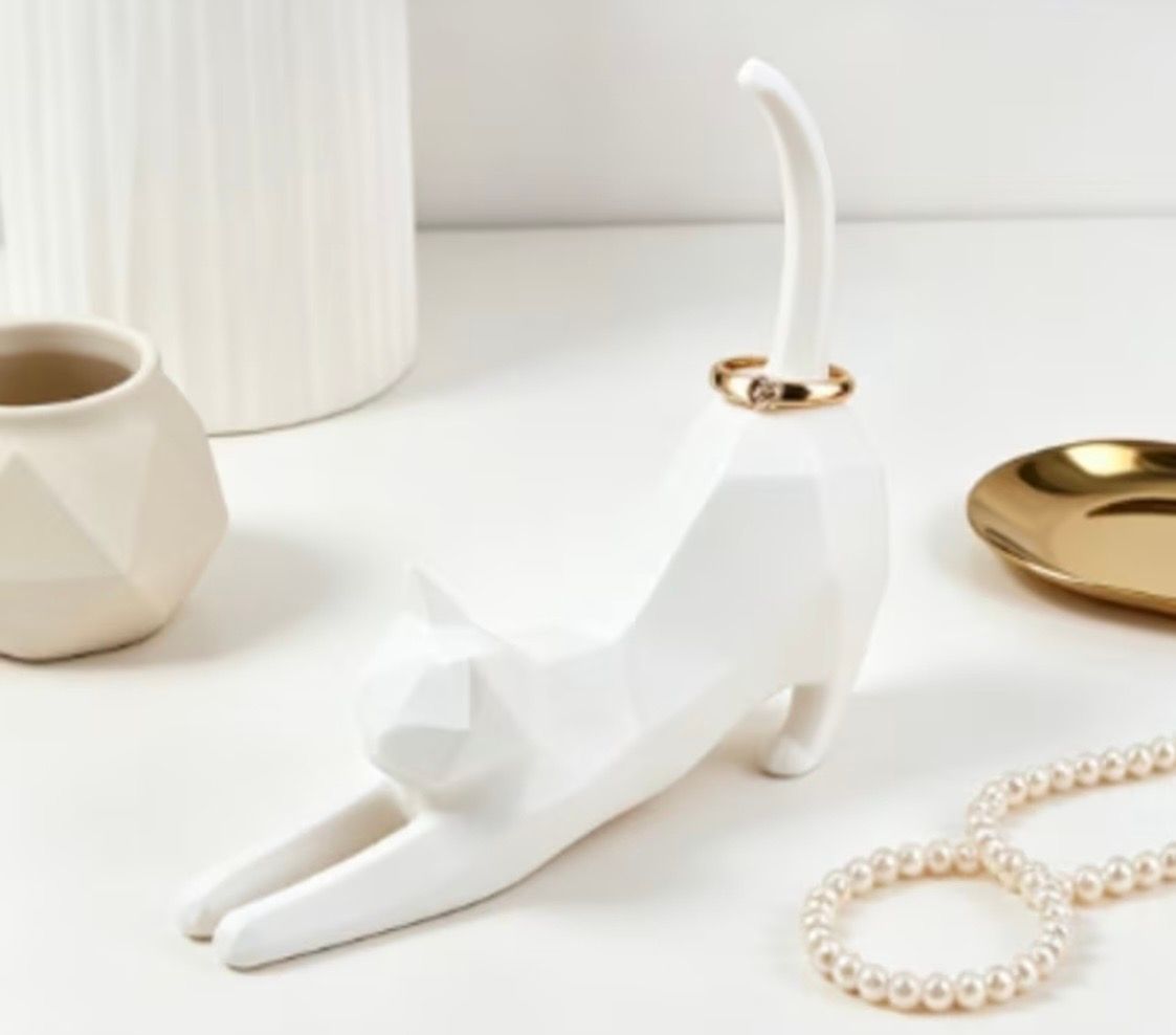 Two cat-shaped ring holders, one white and one black, with rings beside an open jewelry box
