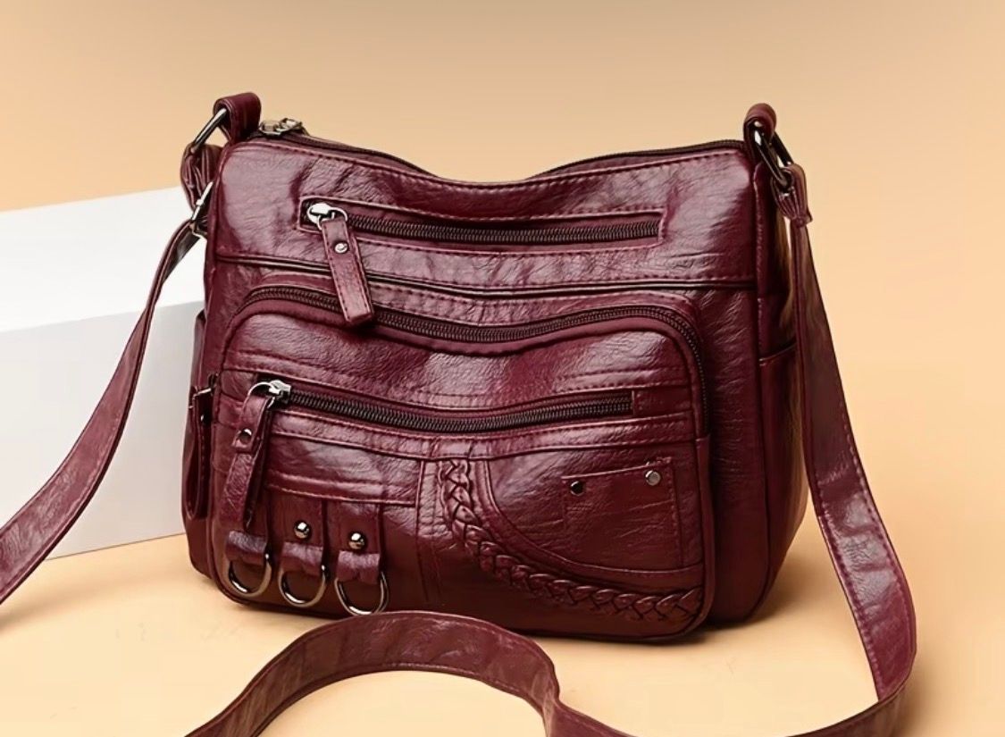 Burgundy leather crossbody bag with multiple zip pockets on a beige background