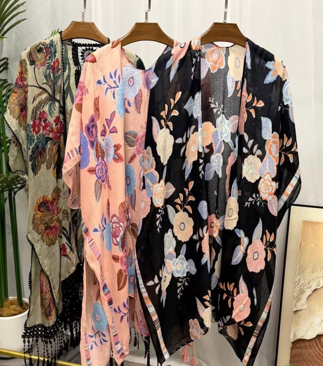 Three floral-patterned kimono-style robes on hangers in soft pink, black, and olive tones