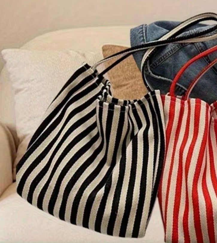 Blue-and-white striped tote bag with black handles hanging against a plain wall