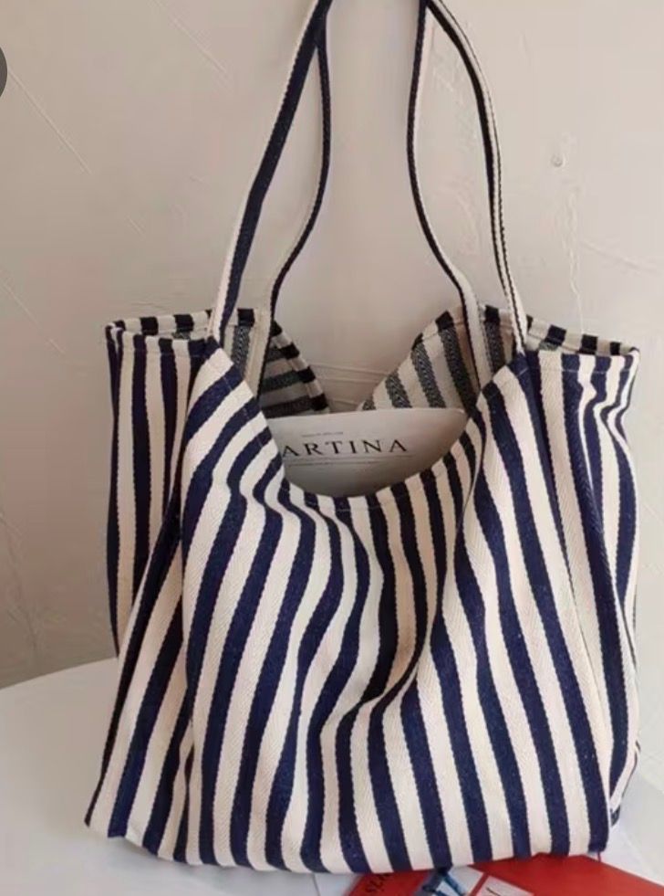 Blue-and-white striped tote bag with black handles hanging against a plain wall